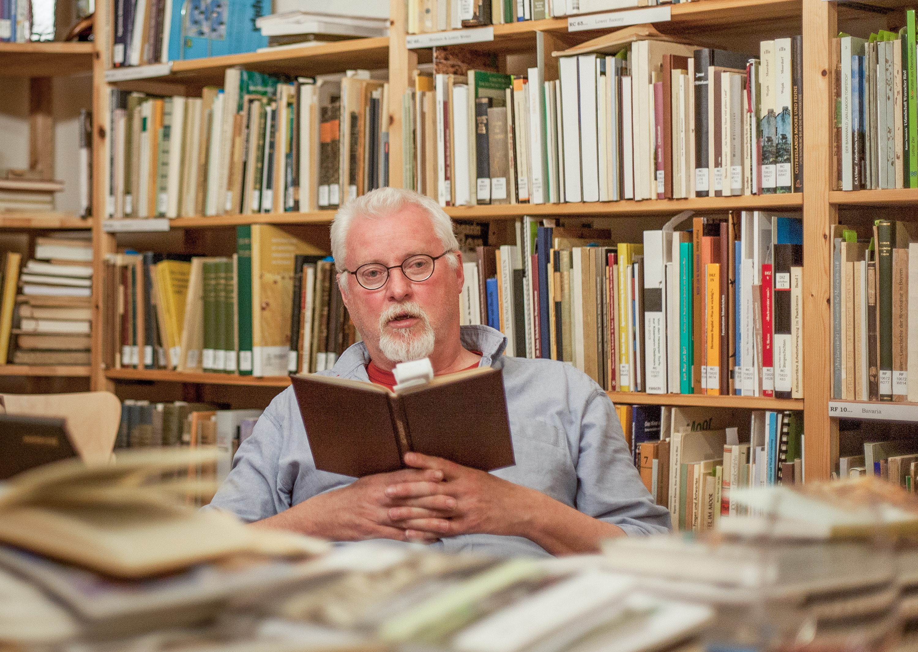 Auf dem Bild sitzt Hans Joosten mit einem Buch in der Hand in der Moorbibliothek