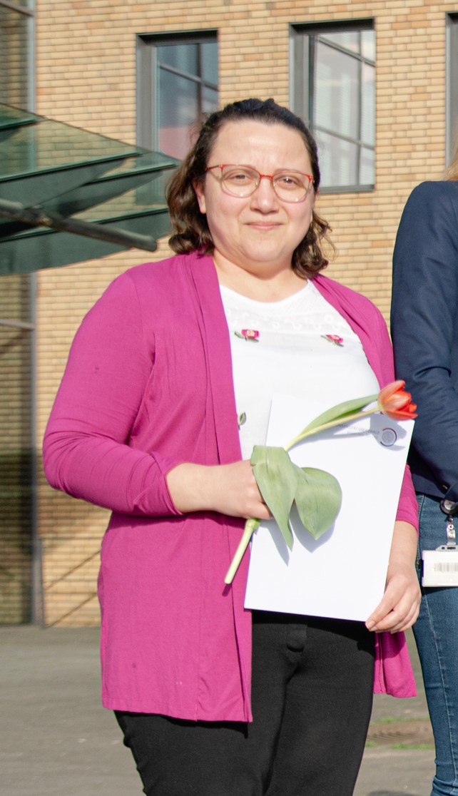 Zu sehen ist Dr. Ruba Al Abdulla. Sie hält ein Zertifikat und eine Blume in der Hand.