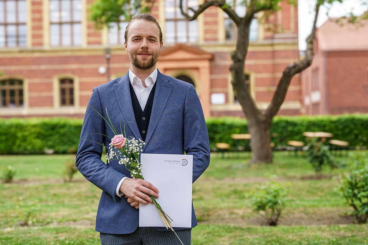 Dr. Max Georg Hügel Max Georg Hügel steht im begrünten Innenhof des Campus Loefflerstraße.