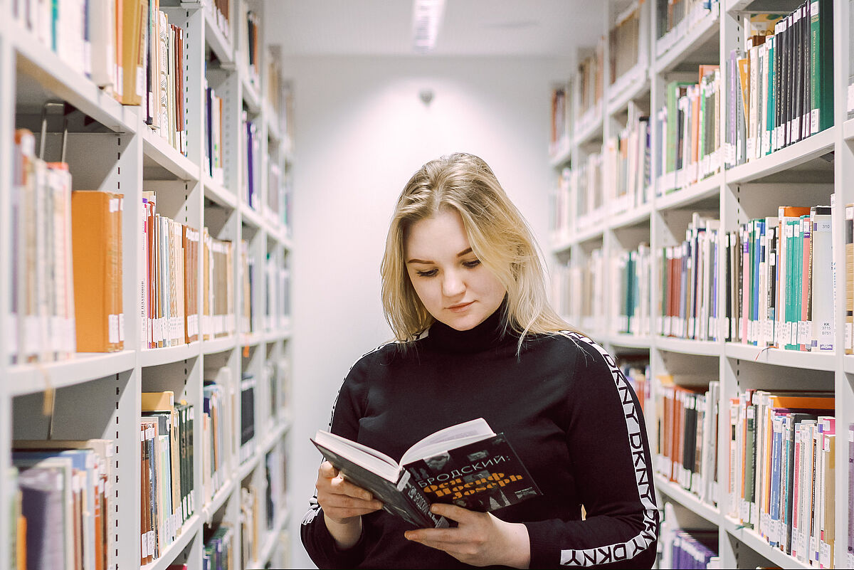 Auf dem Foto sieht man eine junge Studentin, welche ein Buch zur russischen Sprache liest. 