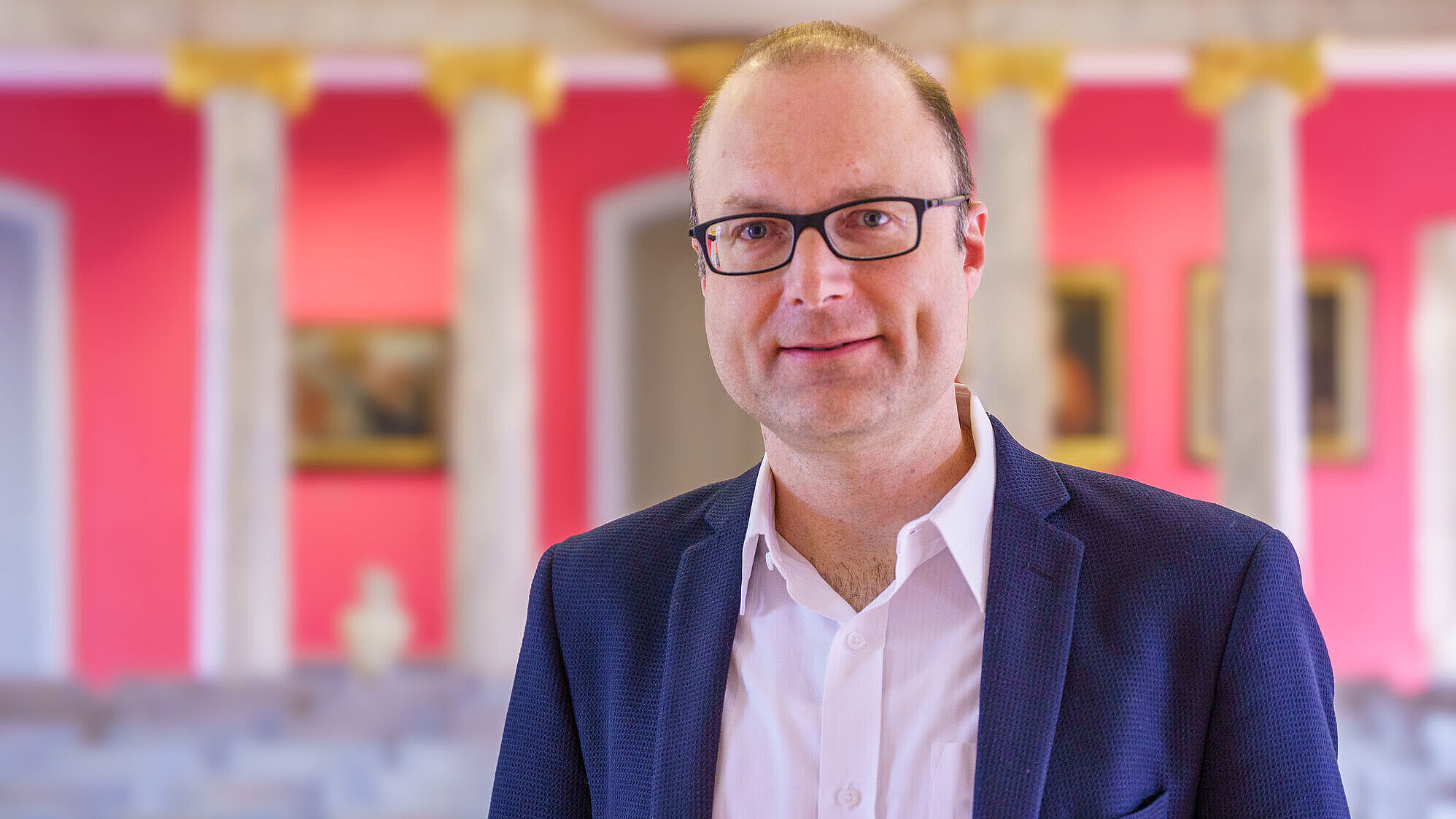 The photo is a portrait of Pro-Rector Prof. Dr. Daniel Schiller in the University of Greifswald's Aula