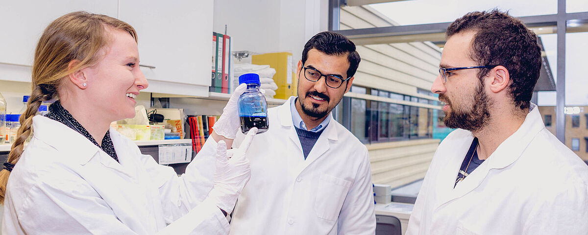 Three doctoral students stand in a lab and talk to each other