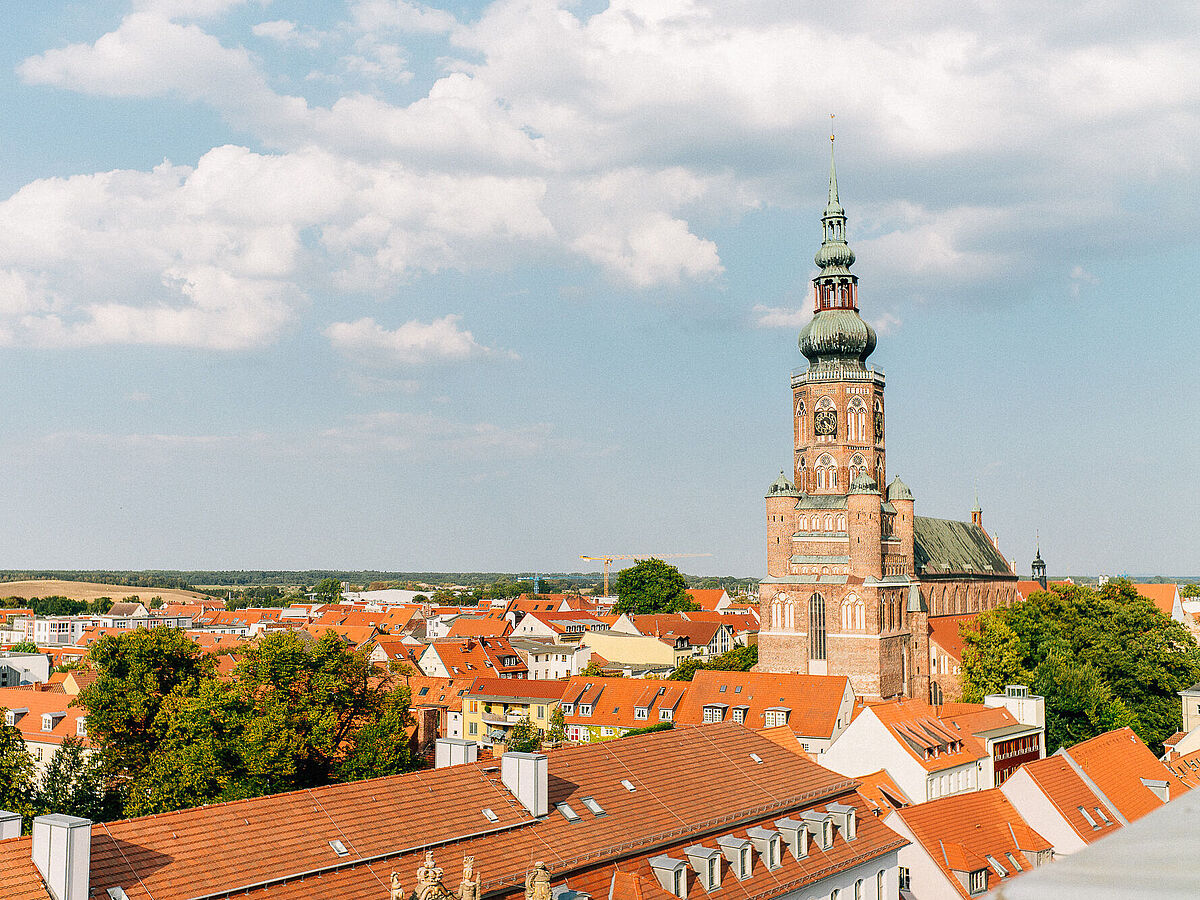 Blick über Greifswalds rote Ziegeldächer der Innenstadt; mittig sichtbar der Dom St. Nikolai mit seinem hohen Turm.