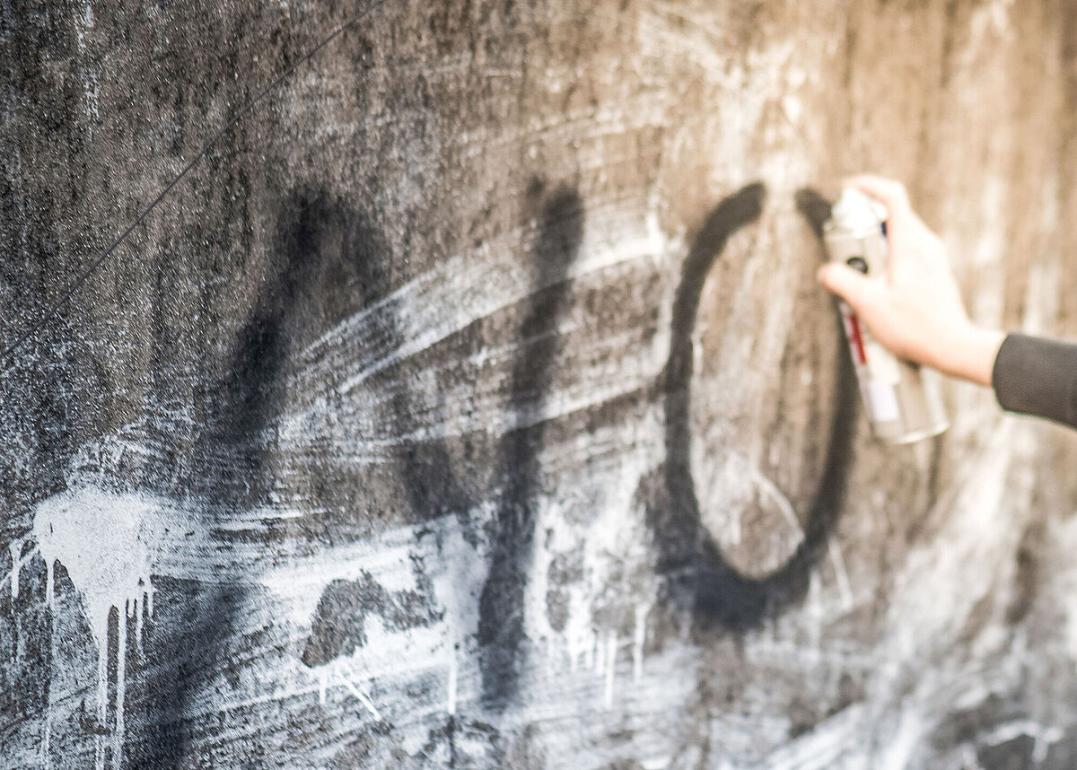 Symbolbild „Keine Graffiti“, © AdobeStock-197054520-zephyrp Eine Hand sprüht den Schriftzug NO an eine verschmutzte Wand.