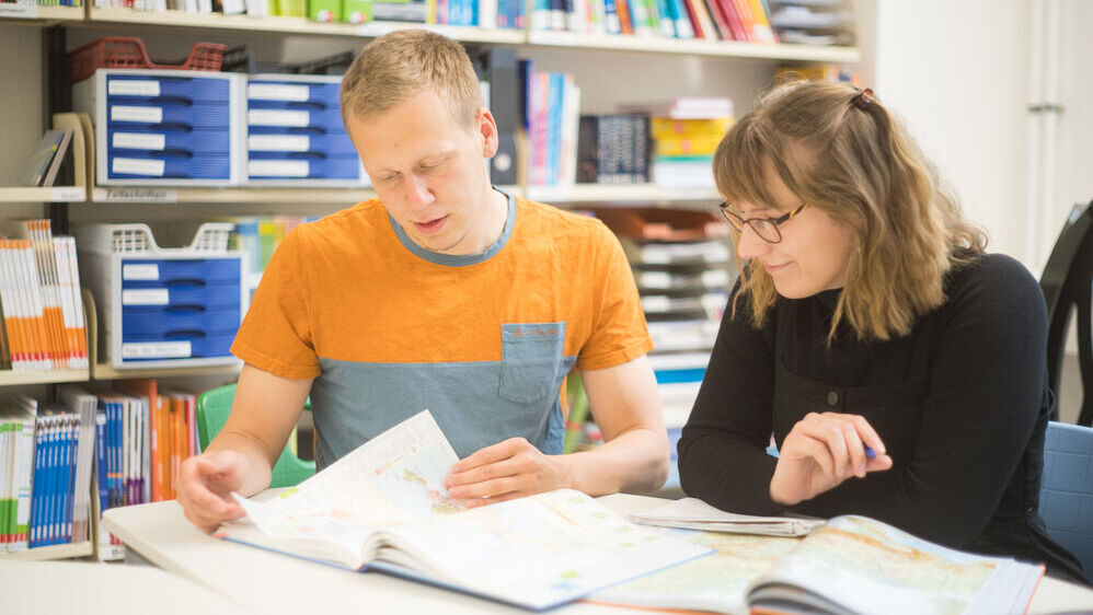 Zwei Personen sitzen zusammen an einem Tisch und bereiten gemeinsam eine Unterrichtsstunde vor. 