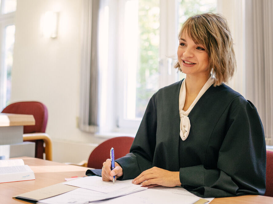 Eine Person im schwarzen Talar arbeitet an einem Tisch im Amtsgericht Greifswald. Vor ihr liegen mehrere Unterlagen.